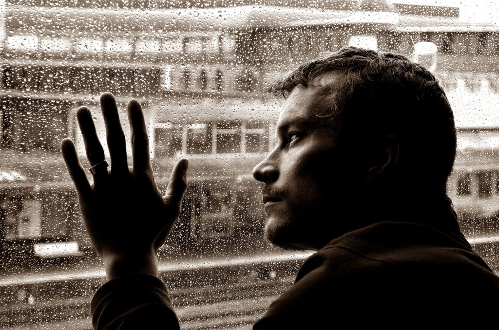 Man with his hand on a rain-drenched window looking sad.