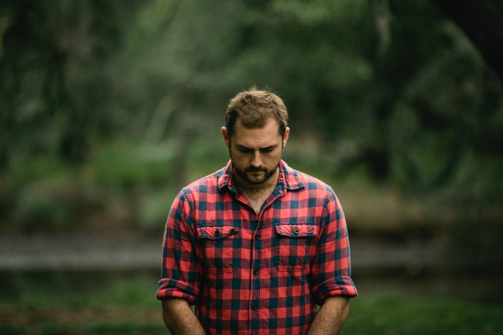 Man in a red and blue checked flannel shirt looking sad.
