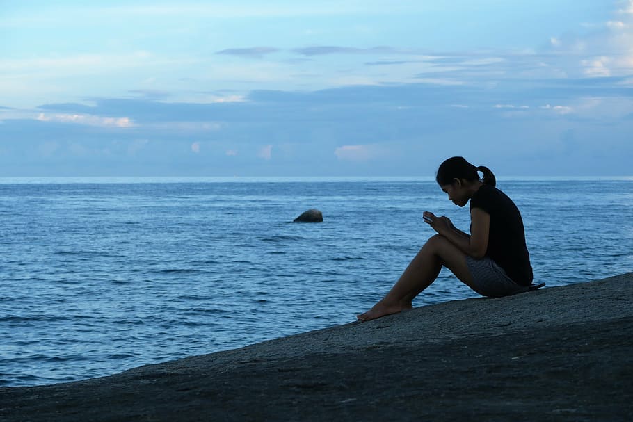 Silhouette of a woman sitting on the seashore at dusk.