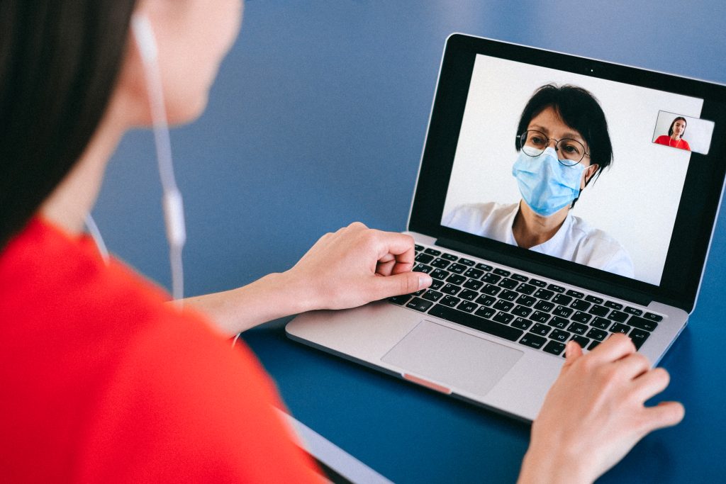 A woman wearing ear phones sitting in front of a laptop computer on a telemedicine consult with a healthcare provider. 