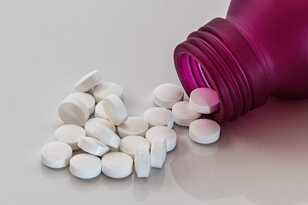 A medication bottle with several round white pills spilling out of it.
